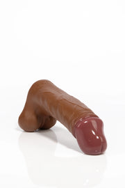 A product photo of a realistic brown dildo lying down.